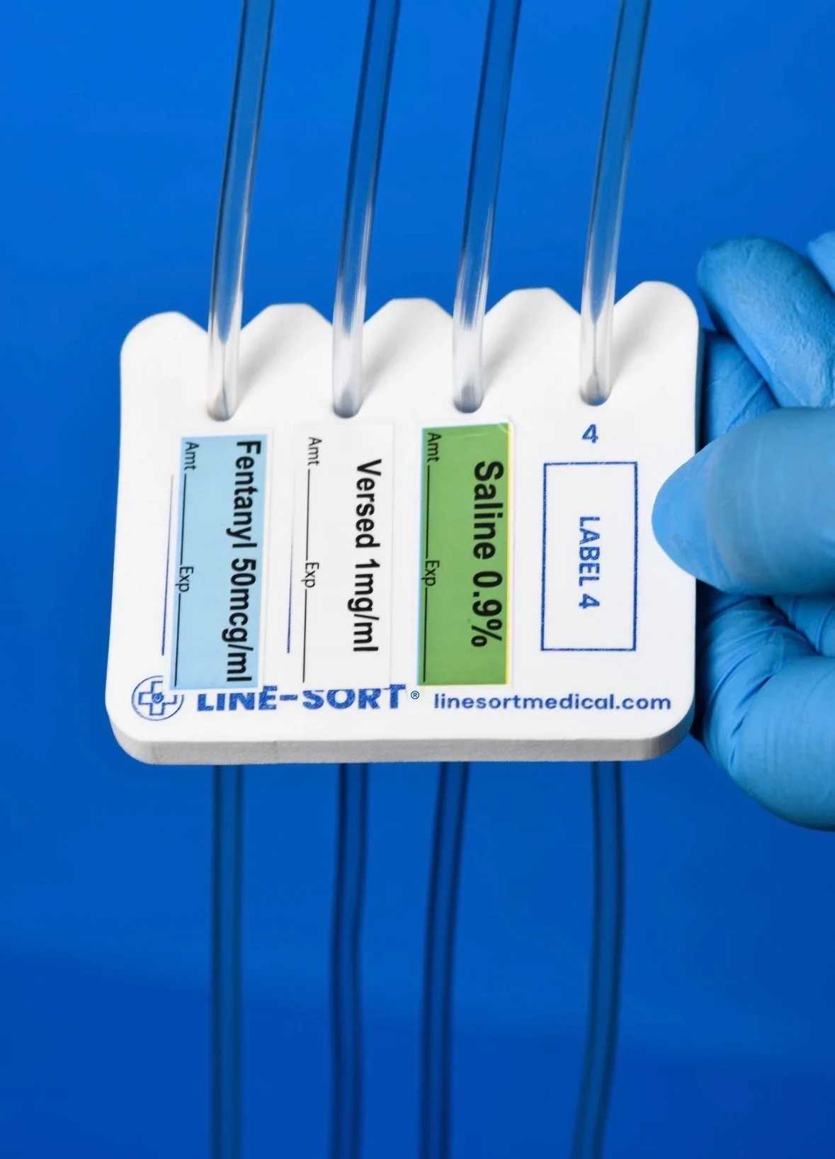 Gloved hand holding a LINE-SORT IV line organizer with three example labels beneath the tubing channels and the fourth label area unfilled